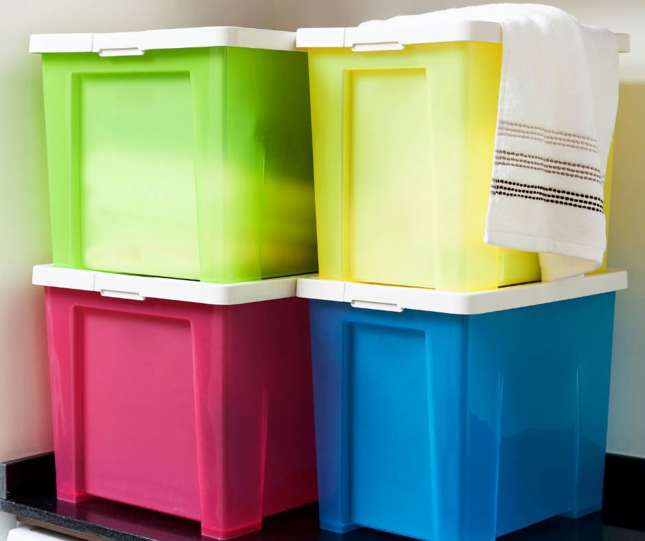 Colorful storage bins stacked in a corner, featuring green, yellow, pink, and blue containers, with a white towel draped over the top bin, ideal for organizing household items.