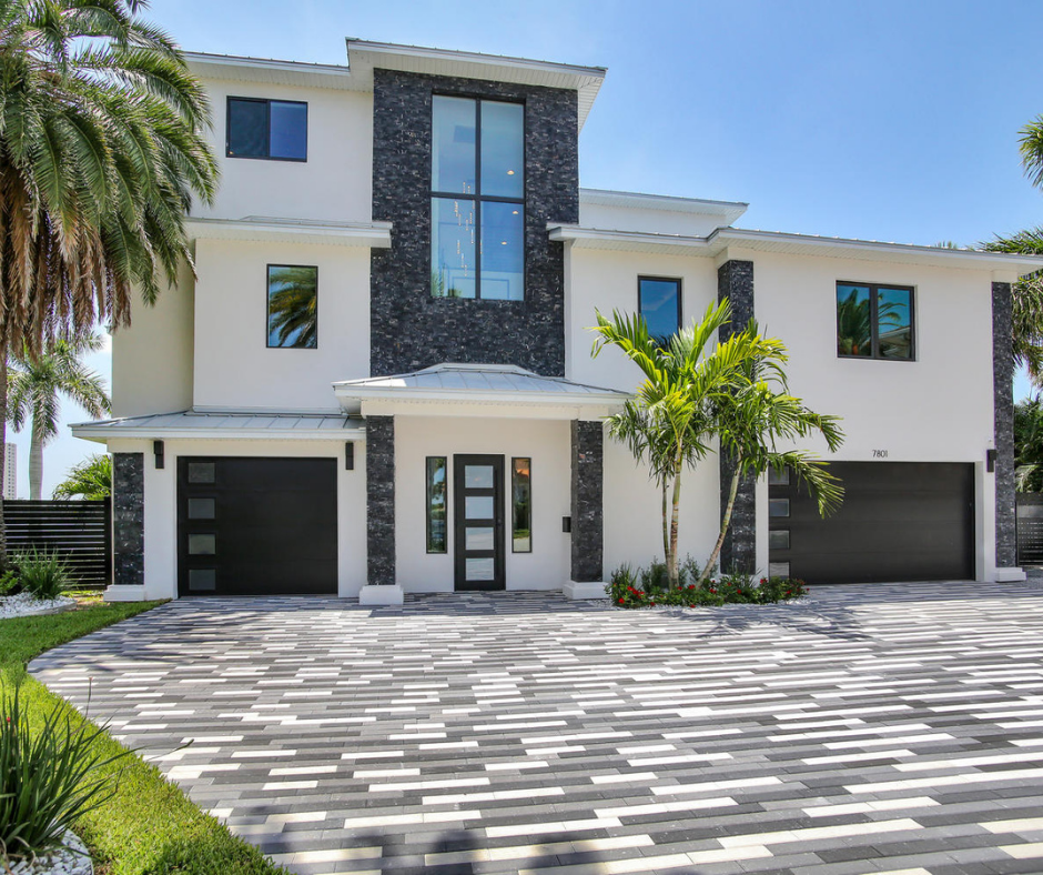 Modern two-story home with a sleek design, featuring dark stone accents and large windows. The property includes a landscaped front yard with palm trees and a stylish paver driveway, enhancing its curb appeal.