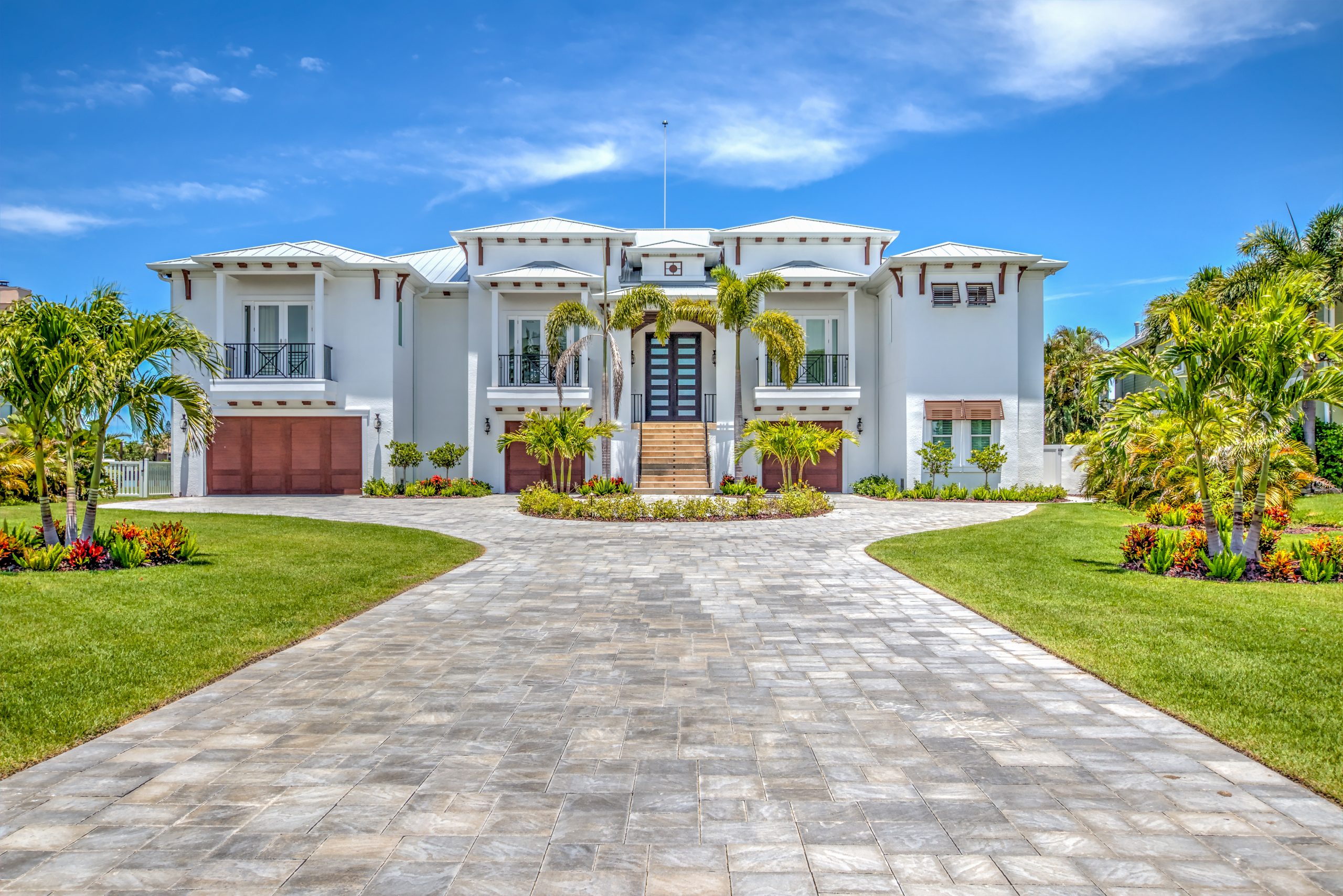 Stunning modern luxury home with a spacious driveway, lush landscaping, and palm trees under a bright blue sky.