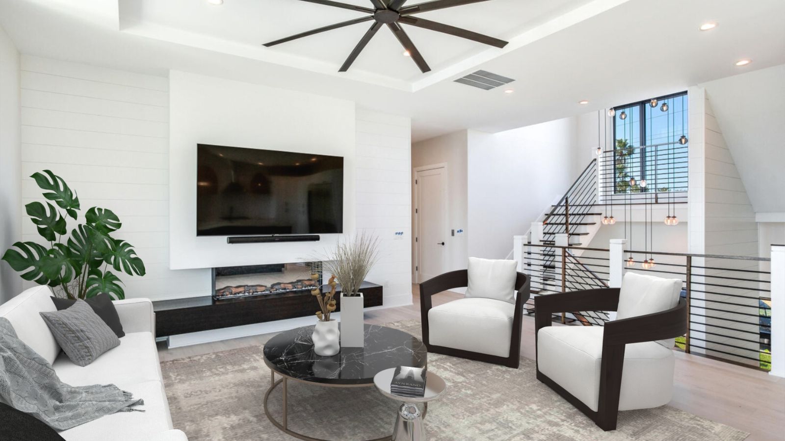 Modern living room featuring a sleek design with a white sectional sofa, black marble coffee table, and stylish armchairs. The space includes a large flat-screen TV mounted on a white wall, a decorative plant, and a contemporary staircase with stylish lighting. Bright, airy atmosphere with ample natural light.