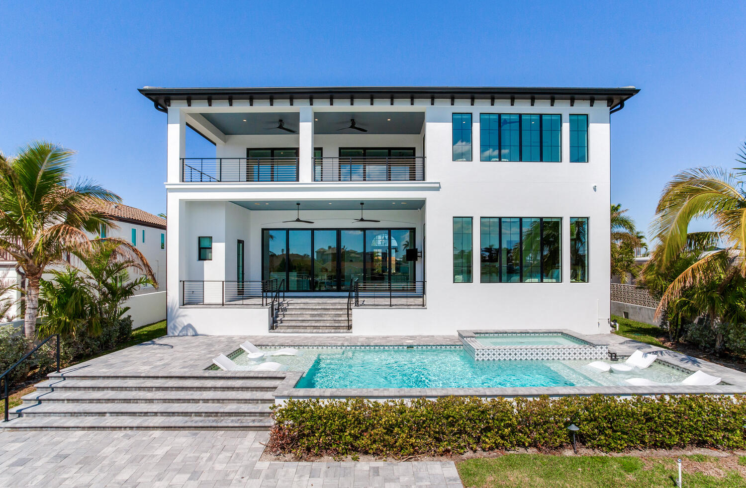 A white home surrounded by palm trees, featuring a sparkling pool in the foreground.