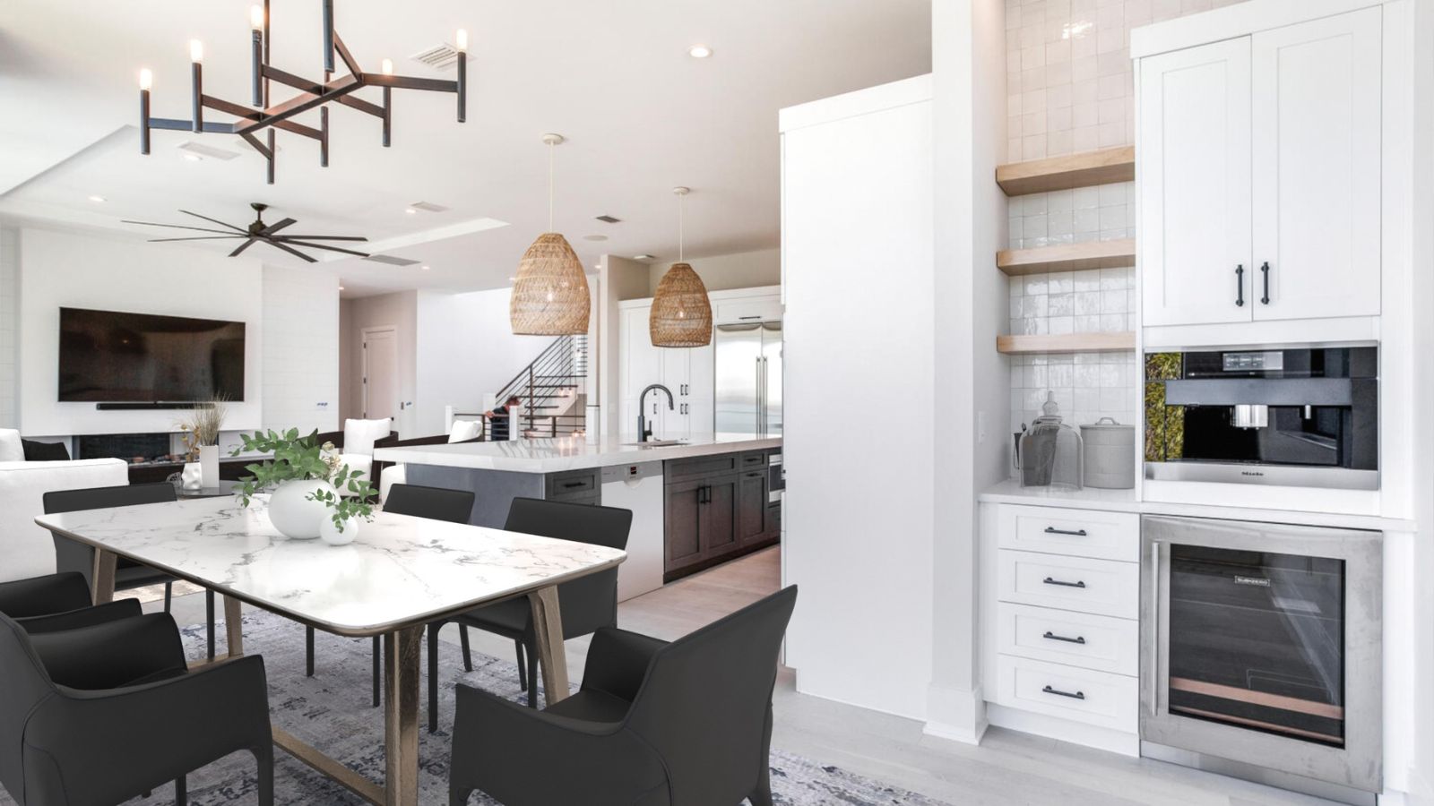 Modern open-concept kitchen and dining area featuring a marble dining table, black chairs, pendant lighting, and a sleek kitchen with stainless steel appliances and white cabinetry. The space is bright and airy, enhanced by a stylish chandelier and decorative elements.