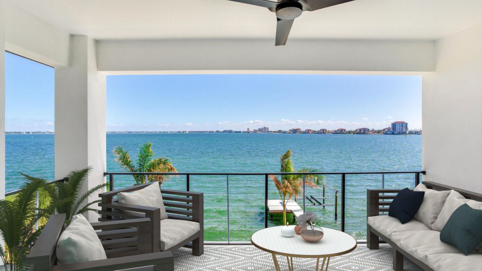Cozy balcony with modern outdoor furniture overlooking a serene waterfront view, featuring lush greenery and a clear blue sky. Ideal for relaxation and enjoying picturesque sunsets.