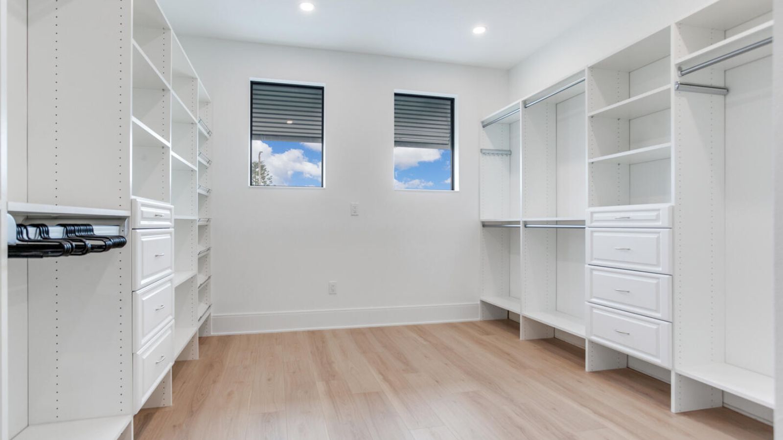Spacious modern walk-in closet featuring white shelving, drawers, and natural light from large windows, ideal for organized storage and stylish design.