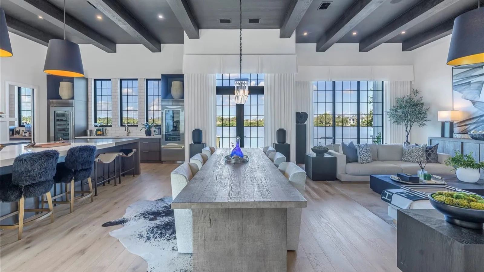 Spacious modern living area featuring a stylish dining table, plush seating, and large windows with scenic views. The kitchen showcases sleek cabinetry, a large island with bar seating, and contemporary lighting fixtures, creating an inviting atmosphere for entertaining.