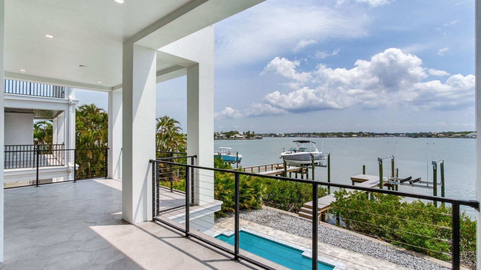 Modern waterfront deck with cable railing, boat dock, private pool, and expansive views of the intercoastal waterway.