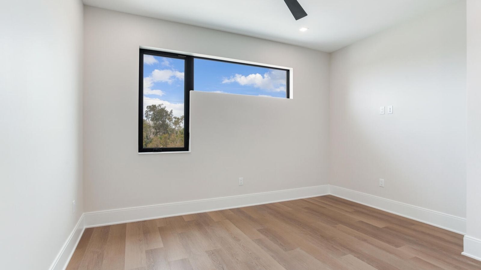 an empty room with hardwood floors, windows and a ceiling fan