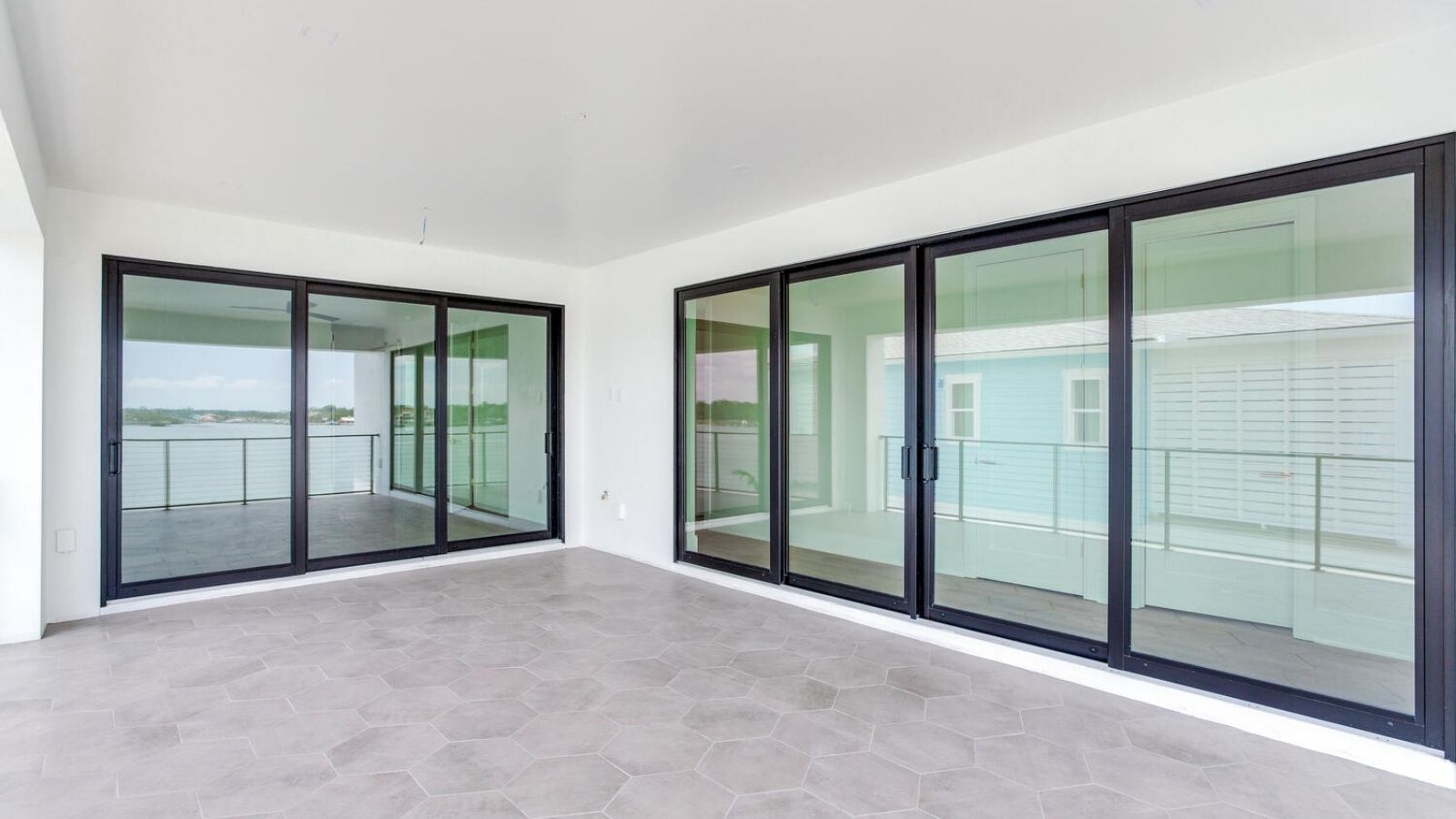modern interior room with large black sliding glass doors, gray hexagonal tile floor, and access to a waterfront balcony