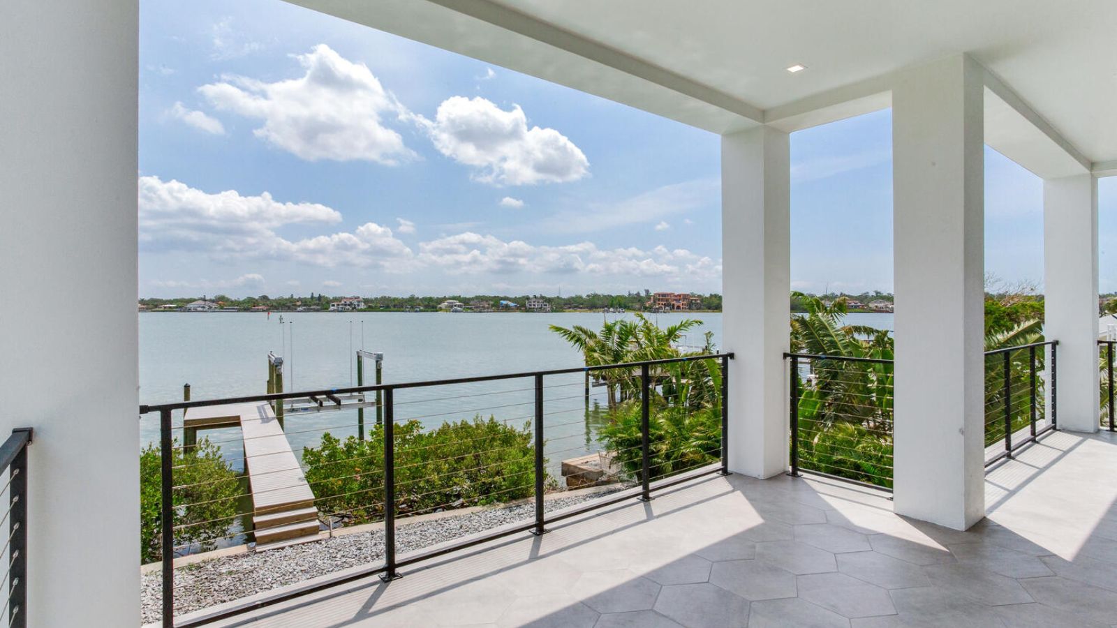 covered waterfront balcony with modern cable railing, hexagonal tile floor, and a view of a private boat lift and intercoastal waterway