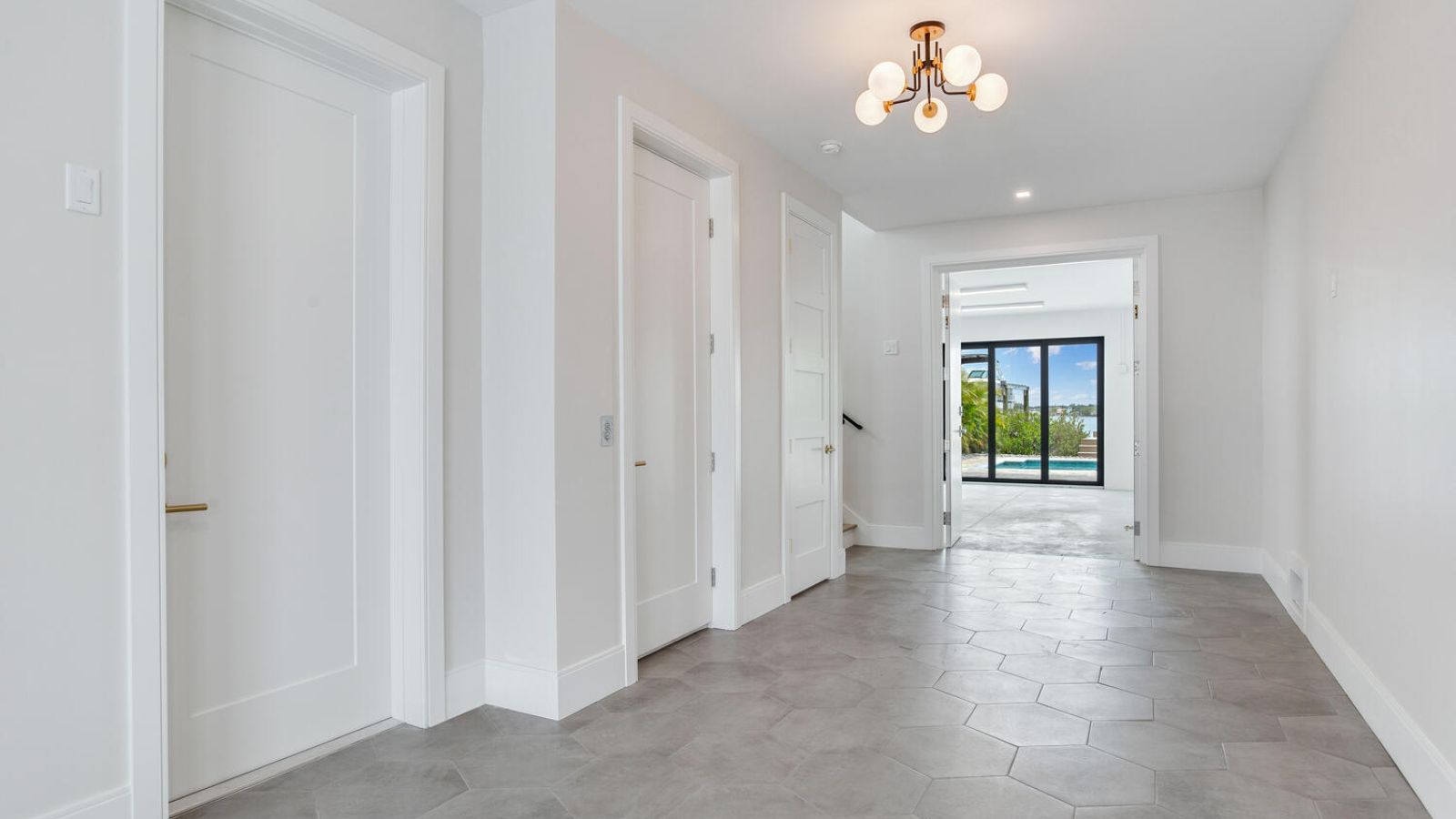 modern interior hallway with gray hexagonal tile floor, white doors with brass hardware, and a view through a doorway to a waterfront pool deck