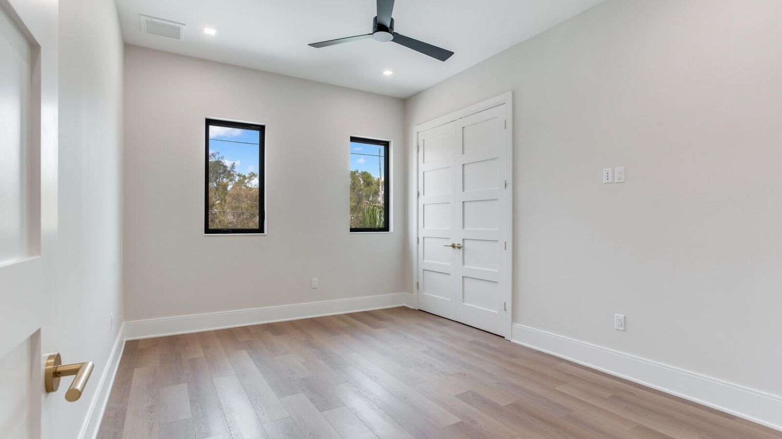 an empty room with hardwood floors, windows and a ceiling fan