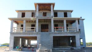 Construction site of a multi-story building featuring a concrete structure, exposed wooden framing, and a staircase leading to the entrance. The image shows scaffolding and construction materials, indicating ongoing work on the property.