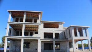 Newly constructed modern building framework with concrete walls and wooden beams under clear blue sky, showcasing three levels and open spaces for windows and doors.