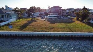 Vacant waterfront lot with a boat parked on a trailer, surrounded by residential homes and palm trees, showcasing potential for development or recreational use.