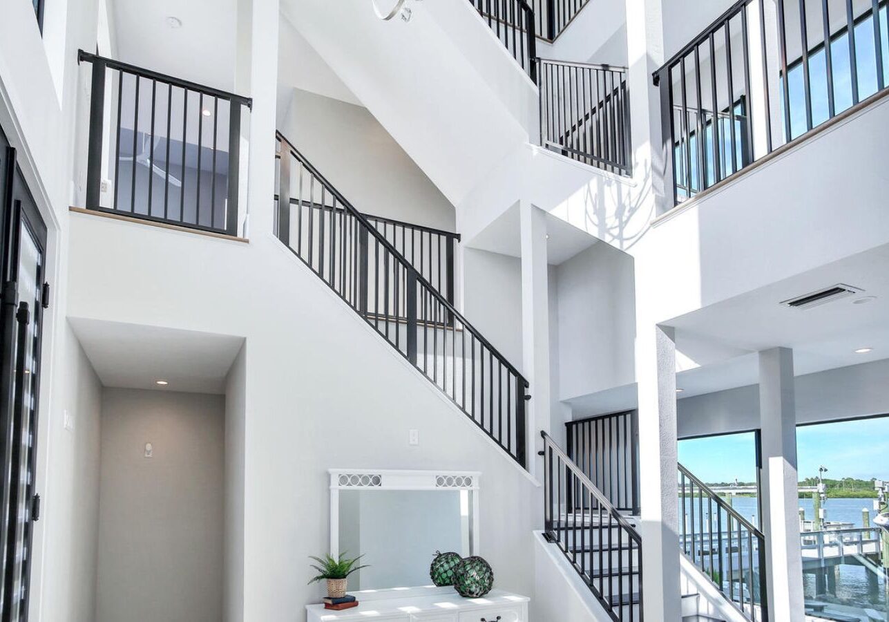 Multi-level interior featuring open staircases, black railings, bright white walls, and modern coastal layout