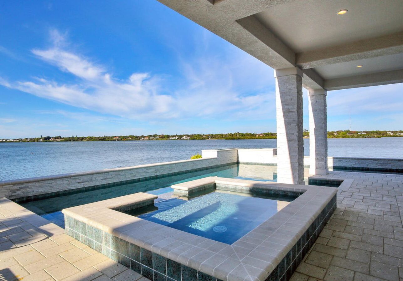 Covered waterfront patio with built-in spa, tranquil water views, and seamless indoor-outdoor living design